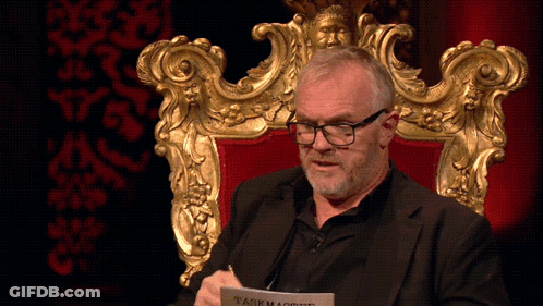 A Man Is Sitting In A Chair With A Piece Of Paper That Says Taskmaster On It GIF
