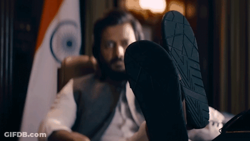 A Man Is Sitting In A Chair With His Feet Up In Front Of A Flag GIF