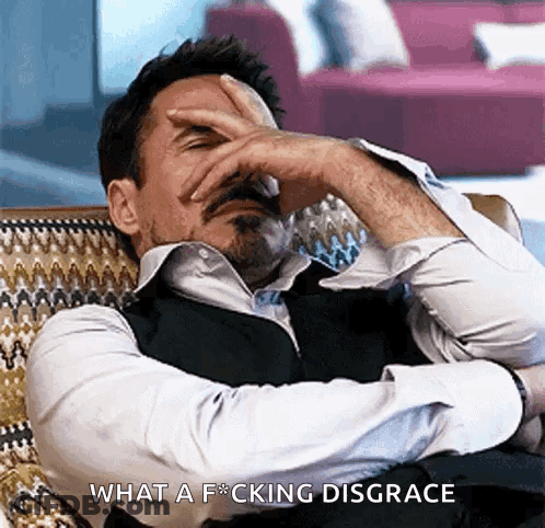 A Man Is Sitting In A Chair With His Hand On His Forehead And The Words What A F * Cking Disgrace Are Above Him GIF