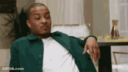 A Man Is Sitting In A Chair With His Hand On His Shoulder . GIF