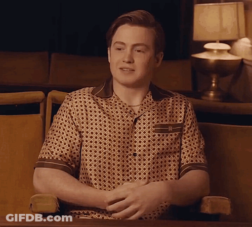 A Man Is Sitting In A Chair With His Hands Folded In Front Of A Lamp GIF