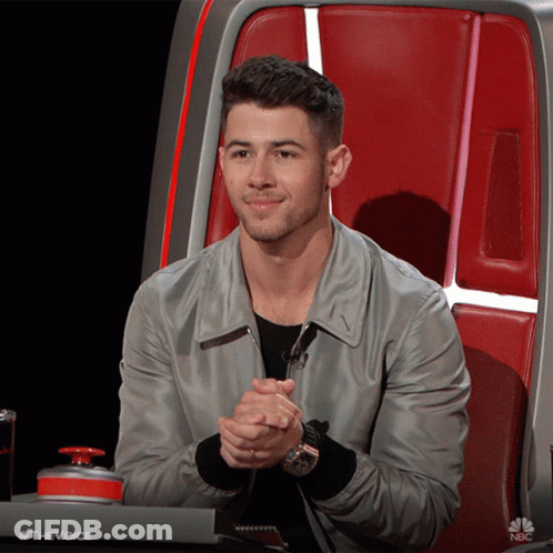 A Man Is Sitting In A Chair With His Hands Folded In Front Of A Nbc Button GIF