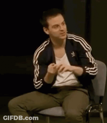 A Man Is Sitting In A Chair With His Hands On His Chest . GIF