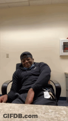 A Man Is Sitting In A Chair With His Hands On His Hips And A Name Tag That Says ' Johnson ' On It GIF