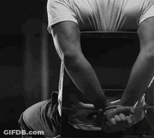 A Man Is Sitting In A Chair With His Hands Tied Behind His Back In A Black And White Photo . GIF