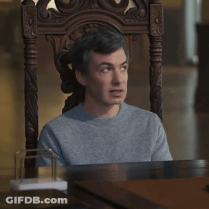 A Man Is Sitting In A Chair With Uhh Sure Written On The Table GIF