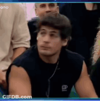 A Man Is Sitting In A Crowd Of People And Looking At The Camera . GIF