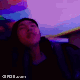 A Man Is Sitting In A Dark Room With A Purple Background And A Foreign Language Written On The Bottom GIF