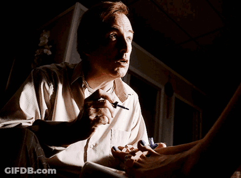 A Man Is Sitting In A Dark Room With A Woman 'S Feet On His Lap GIF