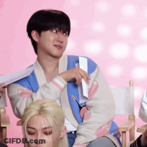 A Man Is Sitting In A Director 'S Chair Holding A Piece Of Paper In His Hand . GIF