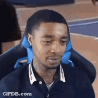 A Man Is Sitting In A Gaming Chair With A Blue Pillow On His Head . GIF