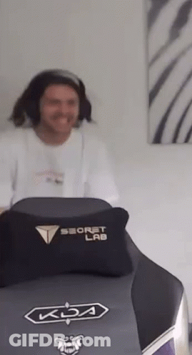 A Man Is Sitting In A Gaming Chair With A Pillow On It . GIF