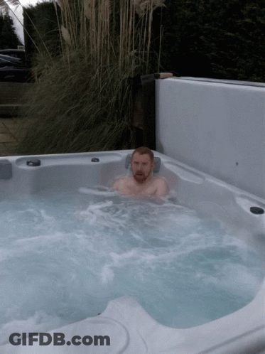 A Man Is Sitting In A Hot Tub With A Plant In The Background GIF