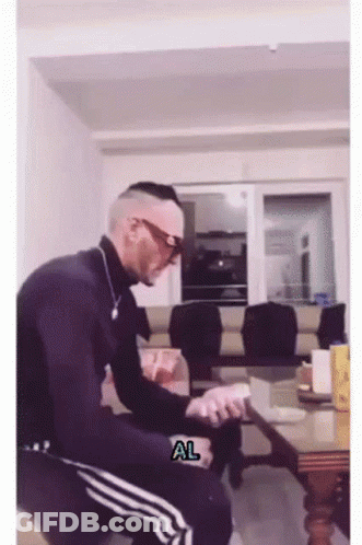 A Man Is Sitting In A Living Room With A Sticker That Says Al GIF
