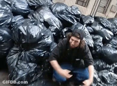 A Man Is Sitting In A Pile Of Garbage Bags . GIF