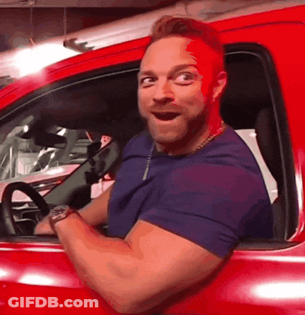 A Man Is Sitting In A Red Car With His Mouth Open GIF
