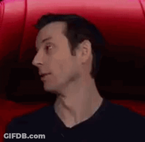 A Man Is Sitting In A Red Chair With His Mouth Open And A Surprised Look On His Face . GIF