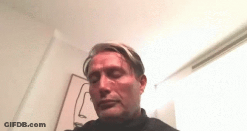 A Man Is Sitting In A Room With His Eyes Closed In Front Of A Painting Of A Face . GIF