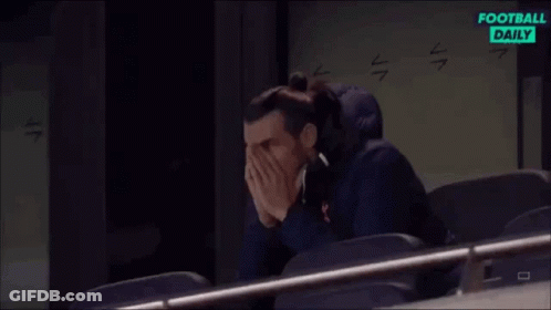 A Man Is Sitting In A Stadium Covering His Face With His Hands While Watching A Football Game . GIF
