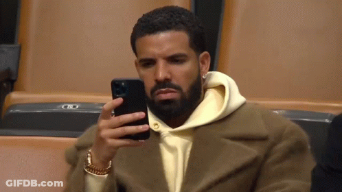 A Man Is Sitting In A Stadium Looking At His Phone . GIF