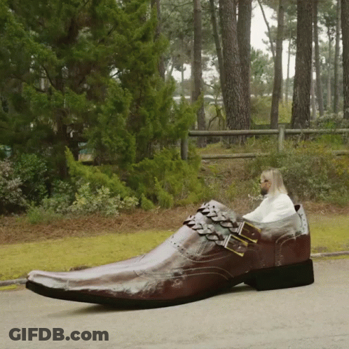 A Man Is Sitting In A Very Large Brown Shoe GIF