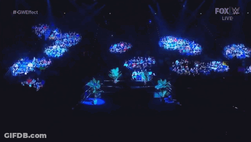 A Man Is Sitting In A Wrestling Ring With Potted Plants . GIF