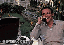 A Man Is Sitting In Front Of A Briefcase And Talking On A Phone GIF