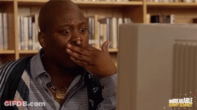 A Man Is Sitting In Front Of A Computer Screen And Covering His Mouth With His Hand . GIF