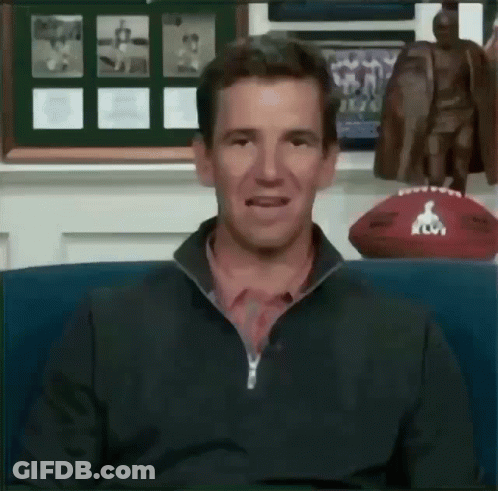 A Man Is Sitting In Front Of A Football And A Statue Of A Man . GIF