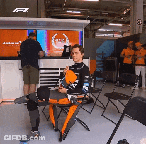 A Man Is Sitting In Front Of A Mclaren Sign GIF