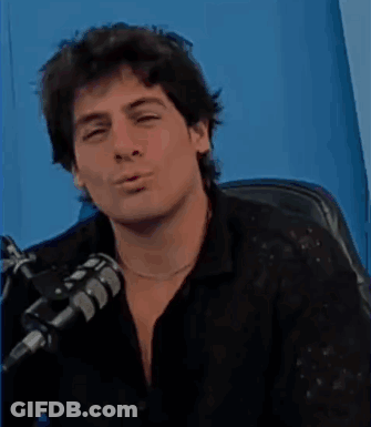 A Man Is Sitting In Front Of A Microphone And Looking Down . GIF