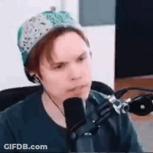 A Man Is Sitting In Front Of A Microphone Wearing A Hat And Headphones . GIF