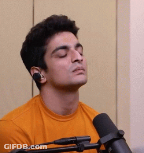 A Man Is Sitting In Front Of A Microphone With His Eyes Closed And Wearing Headphones . GIF