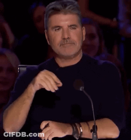 A Man Is Sitting In Front Of A Microphone With His Hands Folded And A Crowd Behind Him . GIF