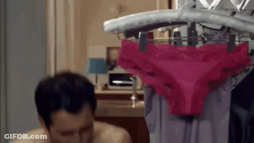 A Man Is Sitting In Front Of A Rack Of Pink Underwear . GIF