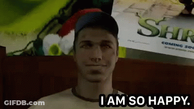 A Man Is Sitting In Front Of A Shrek Poster And Says " I Am So Happy " GIF