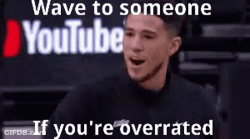 A Man Is Sitting In Front Of A Sign That Says Wave To Someone Youtube If You 'Re Overrated . GIF