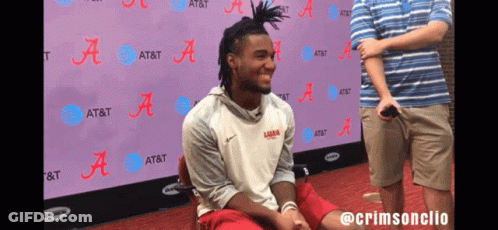 A Man Is Sitting In Front Of A Wall That Says At & T GIF