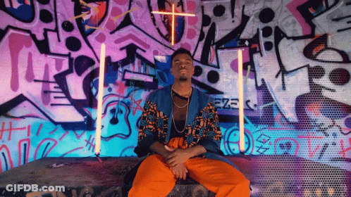 A Man Is Sitting In Front Of A Wall With Graffiti On It That Says Ezz GIF