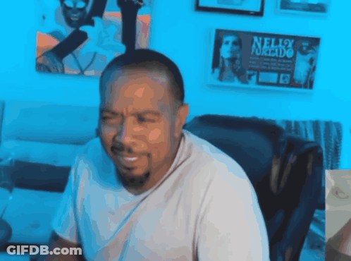 A Man Is Sitting In Front Of A Wall With Nelly Furtado Posters On It GIF