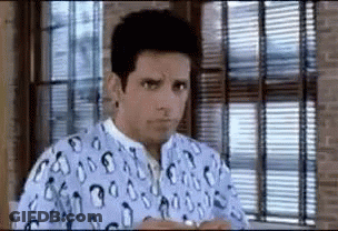 A Man Is Sitting In Front Of A Window Wearing A Hospital Gown . GIF