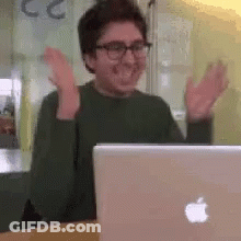 A Man Is Sitting In Front Of An Apple Laptop Computer . GIF