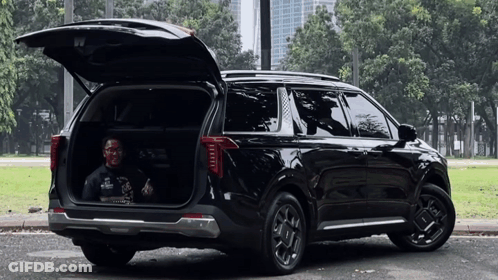 A Man Is Sitting In The Back Of A Black Suv With Its Trunk Open . GIF