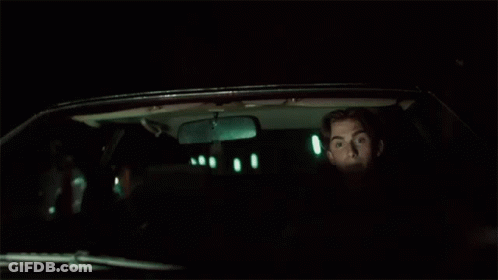 A Man Is Sitting In The Back Seat Of A Car At Night Looking Out The Window . GIF