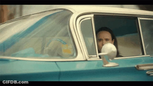 A Man Is Sitting In The Driver 'S Seat Of A Blue Car . GIF