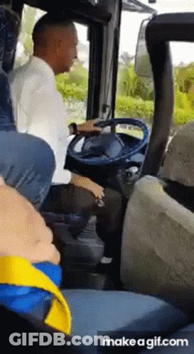 A Man Is Sitting In The Driver 'S Seat Of A Bus While A Child Sits In The Back Seat . GIF