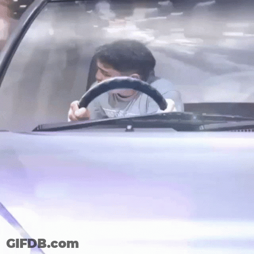 A Man Is Sitting In The Driver 'S Seat Of A Car Holding A Steering Wheel . GIF
