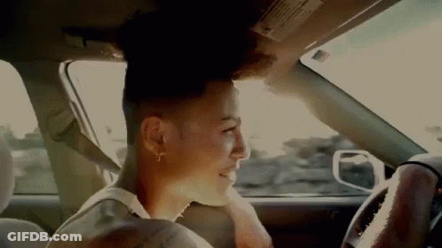 A Man Is Sitting In The Driver 'S Seat Of A Car Looking Out The Window . GIF