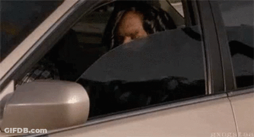 A Man Is Sitting In The Driver 'S Seat Of A Car Looking Out The Window . GIF