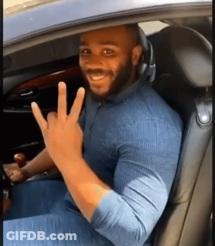 A Man Is Sitting In The Driver 'S Seat Of A Car Making A Peace Sign . GIF